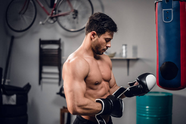 zkušený svalový sportovec se připravuje na souboj, nasazuje si boxerské rukavice. - Fotografie, Obrázek