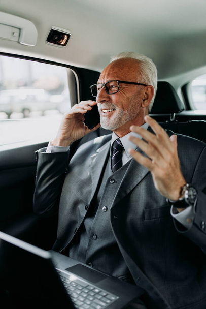 Good looking senior business man sitting on backseat in luxury car. He using his laptop and reacting emotionally. Transportation in corporate business concept. - Photo, image