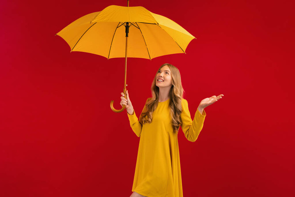 Beautiful happy young woman with yellow umbrella on red background, autumn concept - Foto, Imagen