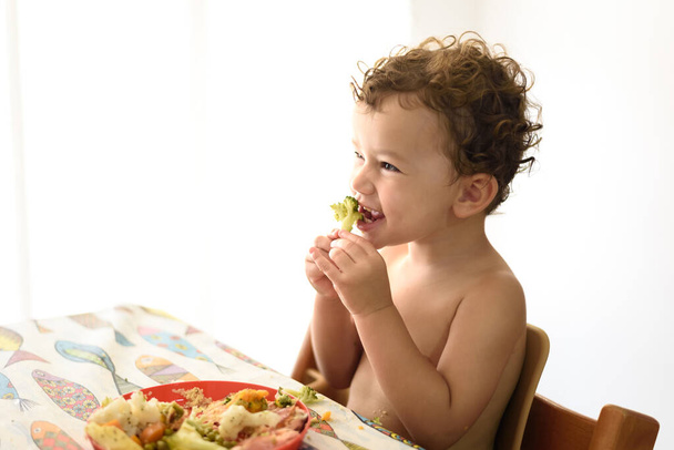 小さな女の子は、空の負のスペースと、ダイニングルームに座って野菜を食べる. - 写真・画像