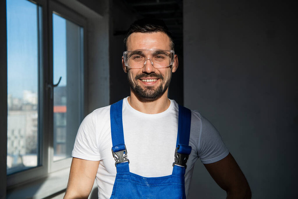 Trabalhador masculino em luvas e óculos sorri gentilmente - Foto, Imagem