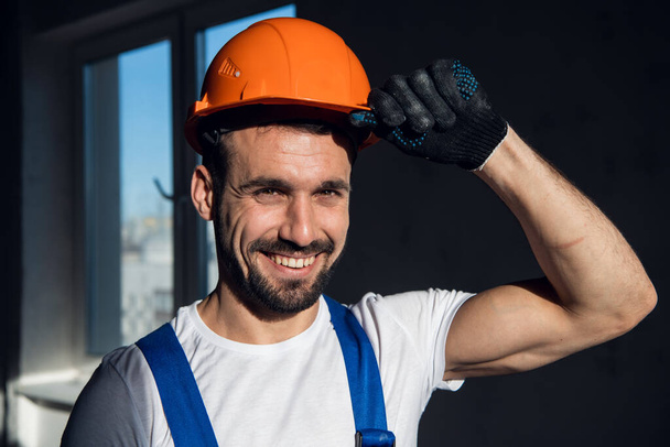 Man in overalls holds on to the visor of a hard hat - Фото, изображение