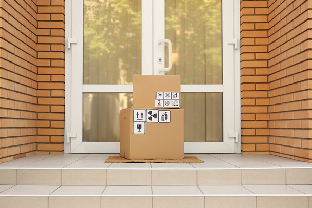 Cardboard boxes with different packaging symbols on door mat near entrance. Parcel delivery - Fotoğraf, Görsel