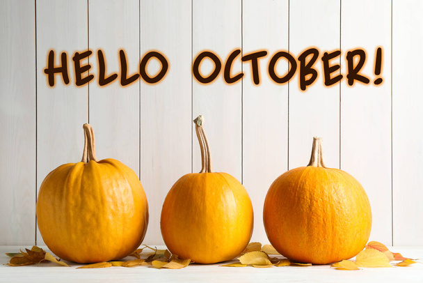 Hello October card. Pumpkins and autumn leaves on white table  - Фото, изображение