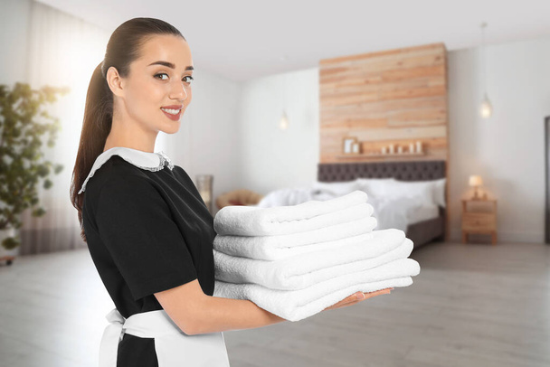 Beautiful chambermaid with clean folded towels in hotel room - Foto, Imagen