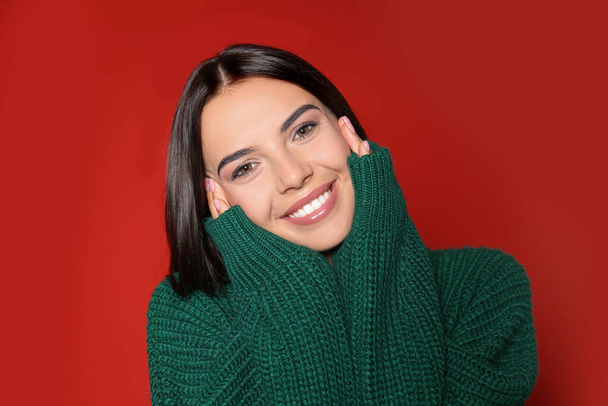 Mujer joven feliz vistiendo suéter caliente sobre fondo rojo - Foto, imagen