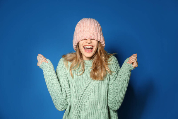 Happy young woman wearing warm sweater and knitted hat on blue background - Фото, изображение