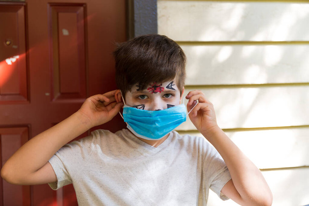 Αγόρι με αποκριάτικο μακιγιάζ φορώντας χειρουργική μάσκα - Φωτογραφία, εικόνα