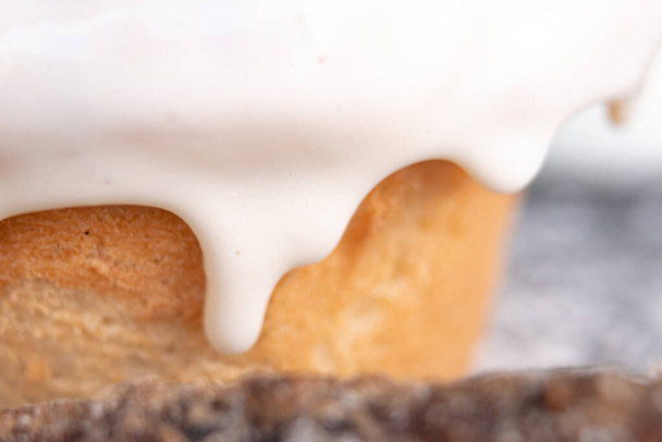 Heerlijk vers gebakken kaneelbroodje bedekt met witte glazuur met een stuk kaneel vooraan met close-up. - Foto, afbeelding
