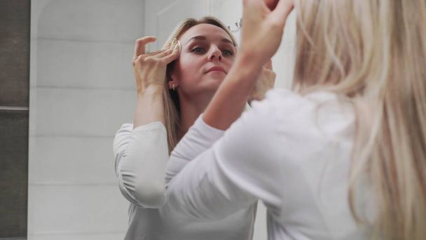 vrouw aanbrengen lotion en kijken in spiegel genieten van natuurlijke schoonheid en gezond - Foto, afbeelding