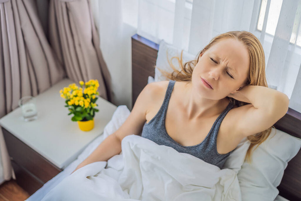 Zdenerwowana młoda kobieta leżąca rano w łóżku odczuwa ból w szyi po śnie, budzi się z bolesnym nagłym bólem lub sztywnością, niewłaściwą postawą podczas snu. Pojęcie fibromialgii - Zdjęcie, obraz