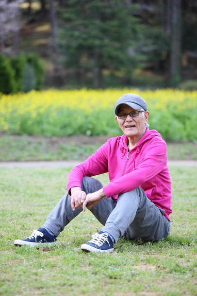 senior Japanese man in pink wear sitting on a lawn - Zdjęcie, obraz