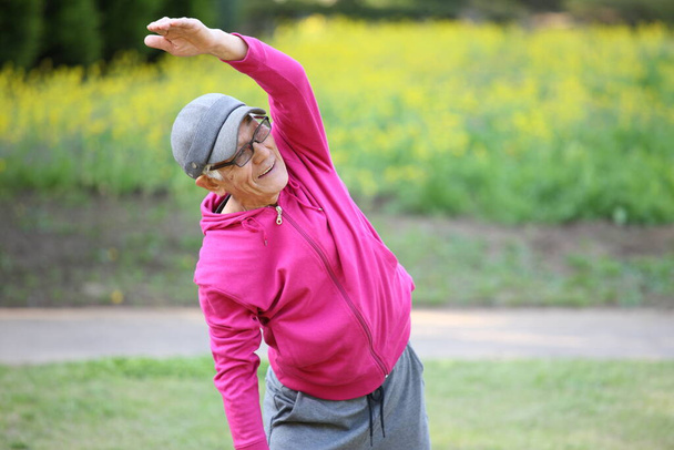 senior Japanese man in pink wear doing standing side bend exercise - Foto, Imagen