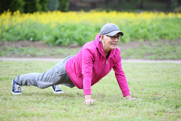 senior Japanese man in pink wear doing push up on a lawn - Фото, изображение