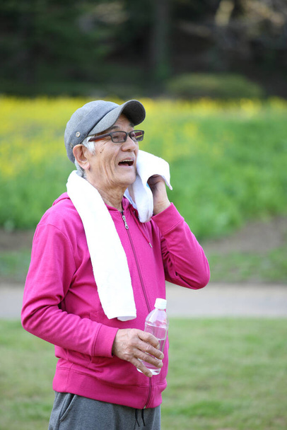 senior Japanese man in pink wear after exercise wiping off sweat outside - Valokuva, kuva