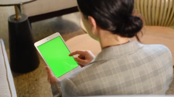 Joven mujer de negocios que utiliza el dispositivo de tableta con pantalla verde. Mujer sosteniendo tableta, páginas de desplazamiento. Vista sobre el hombro. - Metraje, vídeo