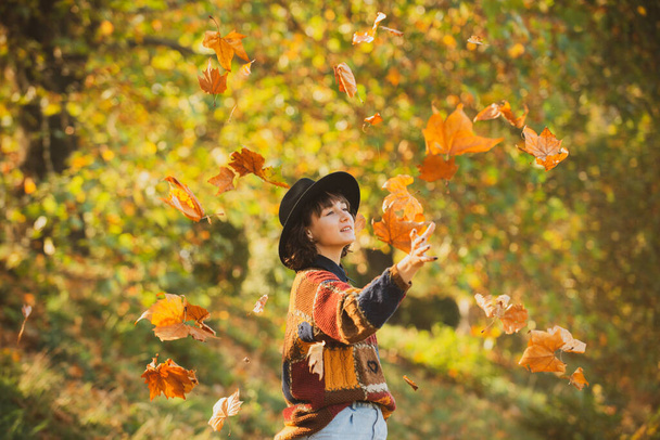 Positive girl model resting. Autumn leaves falling on happy young woman in forest. Fall concept. Autumn woman in autumn park. Beautiful young woman throwing leaves in a park. - Foto, Bild