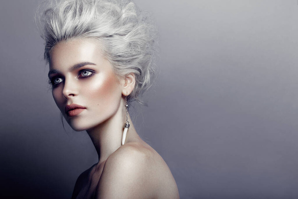 Portrait of stylish young woman with gray hairstyle, smokey eyes and perfect skin and beautiful makeup with naked shoulders, with earring in the ear, looking at one side, isolated on grey background. - Foto, Imagen