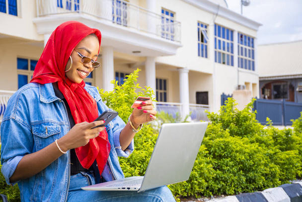An African female sitting outside with her laptop and phone making a payment online - Photo, image