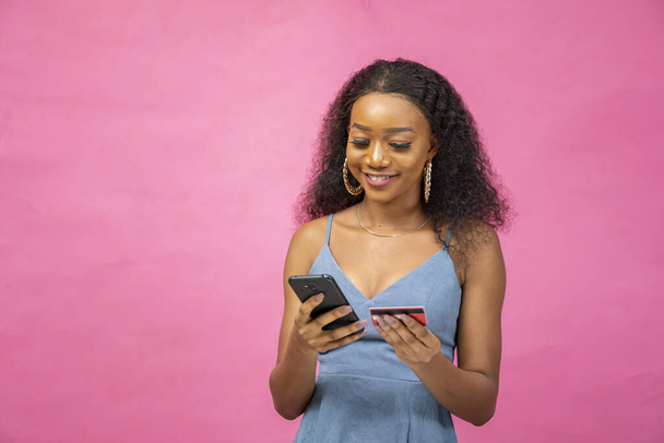 A young African woman putting her credit card information in her cellphone - concept of the online transaction - Foto, afbeelding