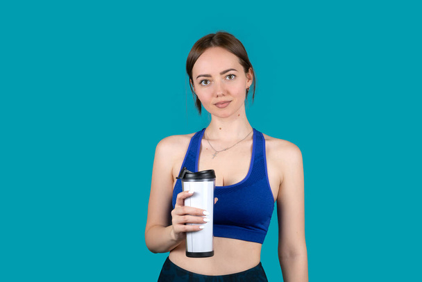 Girl in sports uniform with a cup of water on a blue background - Фото, зображення