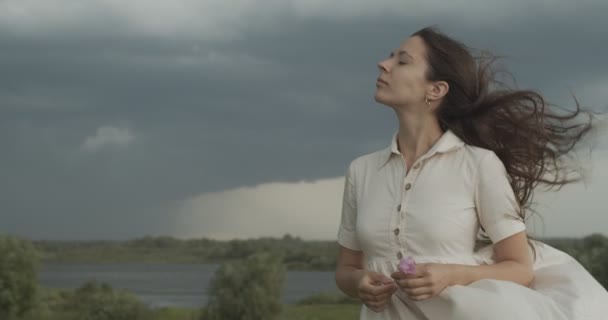 Portrét dívky, jak dýchá čerstvý větrný vzduch na deštivém bouřlivém pozadí oblohy. Vážná žena stojící s foukající chvějící se vlasy venkovní zpomalení kopírovat text prostor. Ochrana životního prostředí - Záběry, video