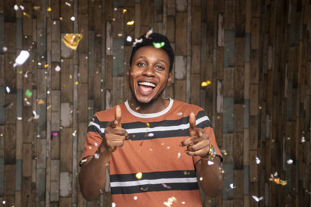 Egy boldog afrikai férfi, aki konfettivel ünnepel egy fafal előtt. - Fotó, kép