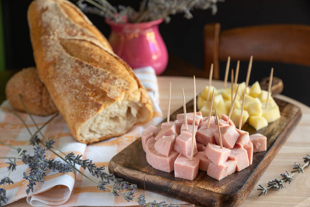 Angri, Italy. Rustic charcuterie board arrangement with mortadella and Italian cheese with toothpick, with bread on wooden cutting board and lavender sprigs. Typical Italian aperitivo food. - Photo, Image