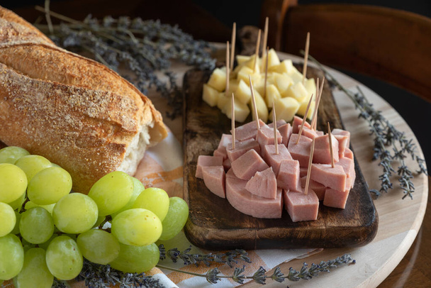 Angri, Olaszország. Rustic charcuterie board elrendezés mortadella és olasz sajt fogpiszkálóval, kenyér fa vágódeszkán, egy csomó szőlő és levendula sprigs. Olasz aperitivo élelmiszer. - Fotó, kép