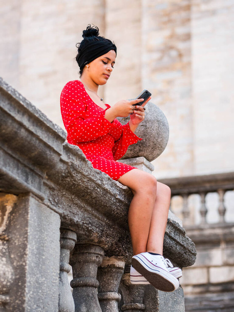 A vertical shot of a young female in red dress with mobile telephone outdoors - Fotografie, Obrázek