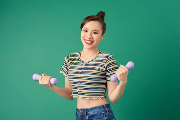 Young Asian woman holding dumbell and wearing casual clothing over green background. - Photo, Image