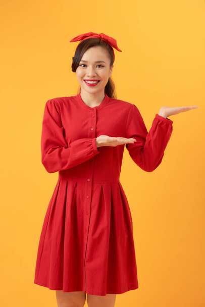 Jeune femme asiatique en robe rouge pointant vers l'espace de copie, isolé sur fond orange - Photo, image