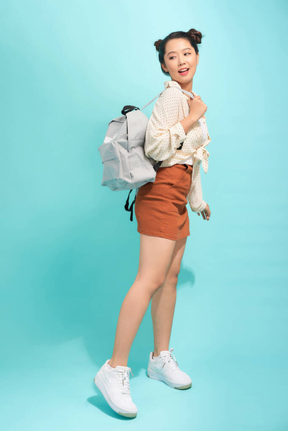 Fashionable young girl holding a backpack, posing isolated on a blue background - Foto, imagen