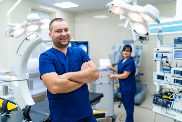 Doctor standing in front of special robotic equipment. Smiling bearded doctor. Woman medic in the background. Hospital and surgery concept. - Foto, imagen