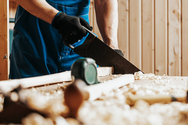 close-up van een bouwvakker die een blok hout zaagt met een handzaag in een werkplaats - Foto, afbeelding