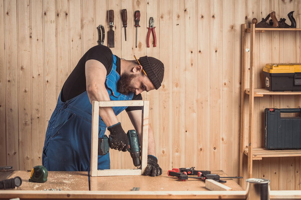 Home repair concepts, close up. Handicraft Carpentry. Cabinet-maker hands drilling a wooden plank using screwdriver on the working table in the workshop - Фото, зображення