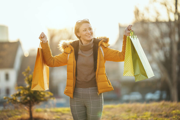 Una joven feliz sonriente está caminando por la calle de una ciudad con bolsas de compras. - Foto, Imagen