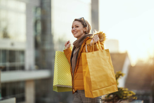 Une jeune femme souriante se promène dans la rue d'une ville avec des sacs à provisions. - Photo, image