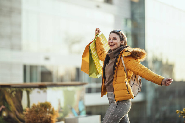 Una giovane donna felice sorridente cammina lungo la strada di una città con le borse della spesa. - Foto, immagini