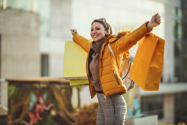 Uma jovem mulher sorridente feliz está andando ao longo da rua de uma cidade com sacos de compras. - Foto, Imagem