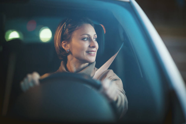 Νεαρή όμορφη ευτυχισμένη γυναίκα κάθεται στο τιμόνι νέο αυτοκίνητο και κοιτάζοντας μέσα από το παράθυρο του αυτοκινήτου.  - Φωτογραφία, εικόνα