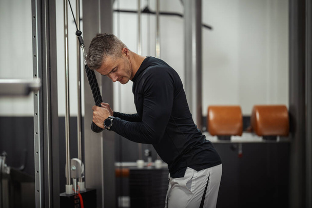 Lihaksikas nuori mies tekee harjoituksia triceps kaapelikoneella voimakoulutuksen aikana kuntosalilla. - Valokuva, kuva