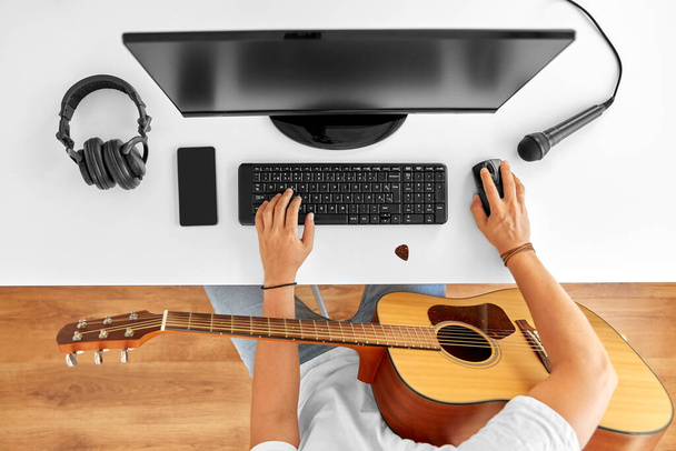 young man with computer and guitar at table - Foto, afbeelding