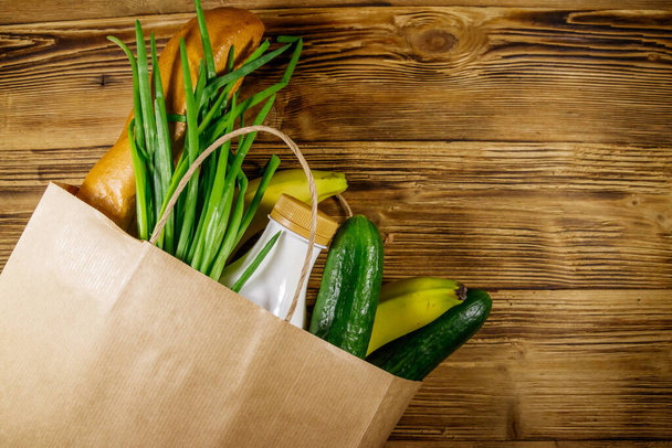 Papiertüte mit verschiedenen Lebensmitteln auf Holztisch. Ansicht von oben. Lebensmitteleinkaufskonzept - Foto, Bild