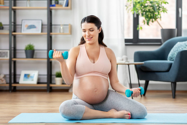 беременная женщина с гантелями занимается спортом дома - Фото, изображение