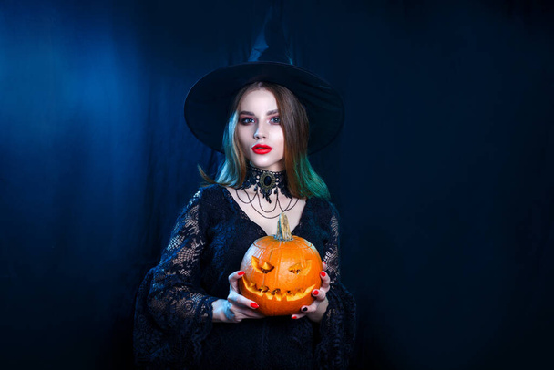 Happy Halloween. Sexy witch holding carved pumpkin on black background - Fotografie, Obrázek