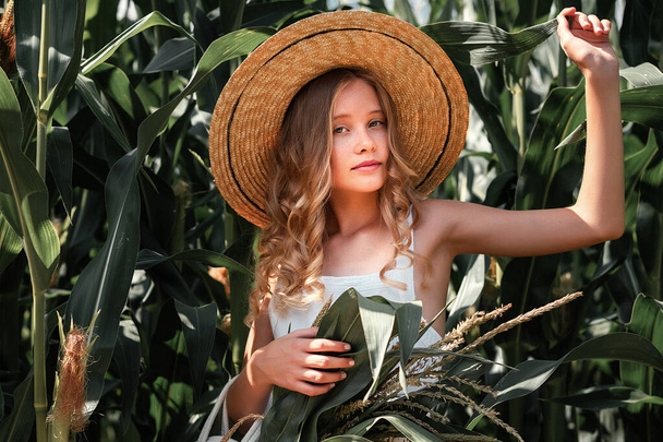 Stylish young girl 10-12 years old in vintage clothing and straw hat posing in a cornfield. Unity with nature. Caring for the environment, calm moment in countryside - Fotó, kép