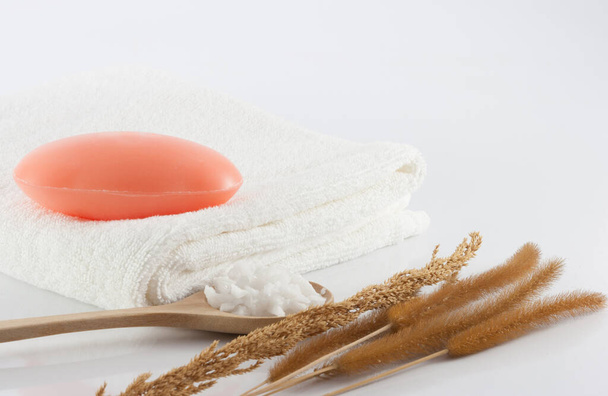 Jabón de barra en toallas blancas limpias, hierba seca y exfoliante de sal en escena blanca para la higiene. - Foto, Imagen