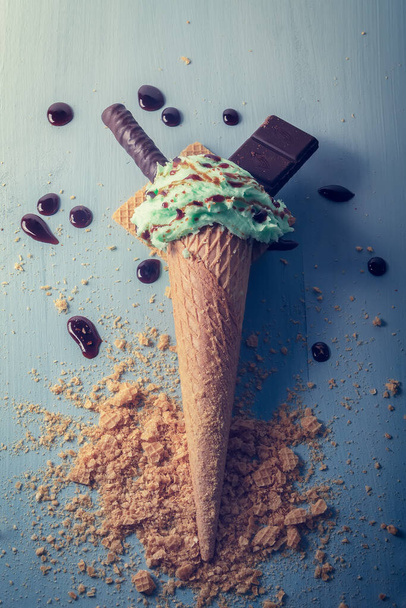 Mint ice cream cone decorated with chocolate, chocolate wafer and caramel syrup. On a light blue wooden background, dark style photography with light warm tones in matte - Fotoğraf, Görsel
