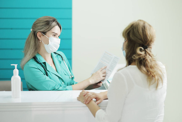 Woman doctor or nurse in a medical mask talks to a female patient - Fotoğraf, Görsel